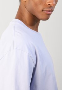 Világoslila pamut póló környakú, rövid ujjú kivitelben, látható varrási részletekkel, oldalnézetben bemutatva.