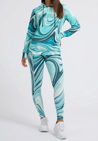 Conjunto de sudadera con capucha y mallas en un patrón veteado en turquesa y blanco. Fabricado con material elástico, con un logo en el pecho y un diseño ajustado.