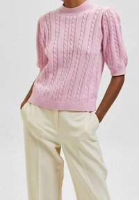 Hellrosa kurzärmliger Pullover mit Zopfmuster und geripptem Ausschnitt, kombiniert mit cremefarbenen, weit geschnittenen Hosen.