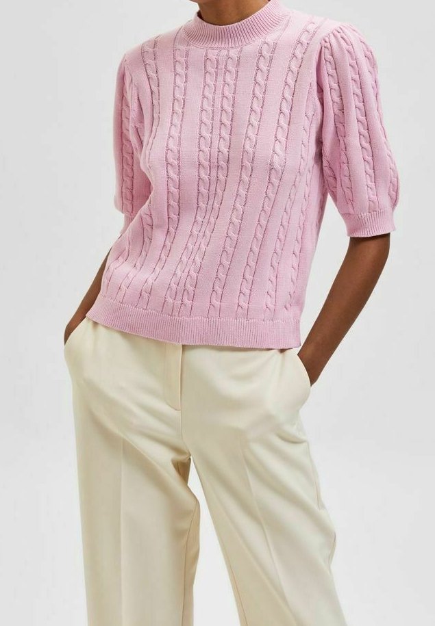 Hellrosa kurzärmliger Pullover mit Zopfmuster und geripptem Ausschnitt, kombiniert mit cremefarbenen, weit geschnittenen Hosen.