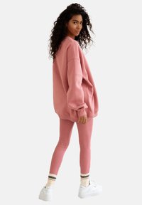 Różowa, oversize'owa bluzę z długim rękawem i dopasowane legginsy w tym samym kolorze, oba z miękkiego materiału, połączone z białymi trampkami i skarpetkami w paski.