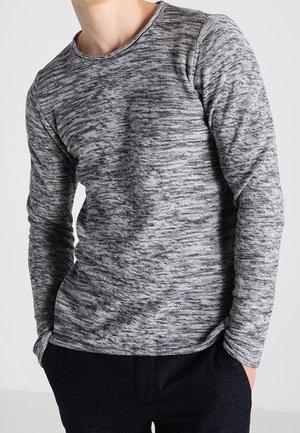 Chemise à manches longues, col rond, en tissu gris texturé avec un motif marbré subtil, associée à un pantalon à carreaux sombres.