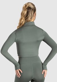 Grøn, langærmet crop top lavet af glat, strækbart stof med en mock neck. Har tætsiddende ærmer og en ren kant.