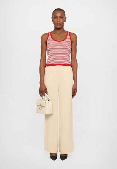 Débardeur rayé rouge et blanc avec un ourlet volanté, associé à un pantalon large crème. Le mannequin tient un petit sac blanc avec une anse circulaire.