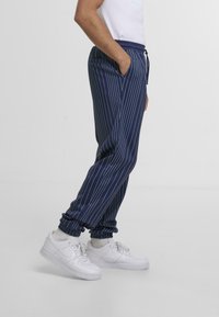 Joggers a righe navy realizzati in un tessuto morbido, con vita elastica, tasche laterali e caviglie a coste, abbinati a sneakers bianche.