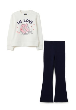 Felpa bianca con sneakers rosa e testo "In Love with this shoes" abbinata a pantaloni neri a campana semplici.