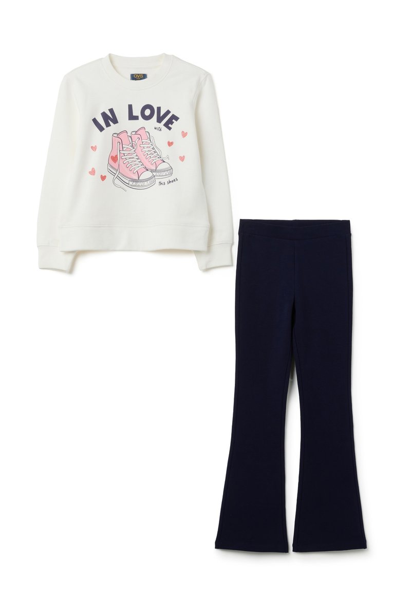 Witte sweatshirt met roze sneakers en de tekst "Verliefd op deze schoenen" in combinatie met eenvoudige zwarte flared broeken.