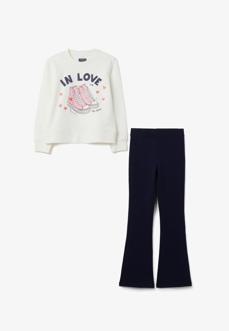 Witte sweatshirt met roze sneakers en de tekst "Verliefd op deze schoenen" in combinatie met eenvoudige zwarte flared broeken.