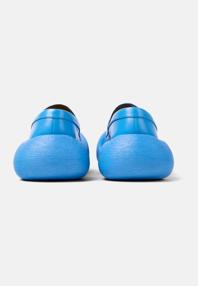 Scarpe in pelle blu con un design rotondo, caratterizzate da una suola texturizzata di un blu chiaro. Le scarpe hanno una parte superiore liscia e uno stile minimalista.