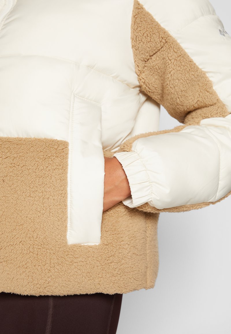 Giacca imbottita con una parte superiore color crema e una parte inferiore in pile color sabbia. Presenta polsini elasticizzati e una tasca frontale. Texture morbida.