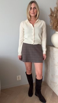 Cardigan écru, mini-jupe à carreaux marron et bottes en suède noires jusqu'aux genoux. Texture lisse et coupe décontractée. Design simple avec des boutons.