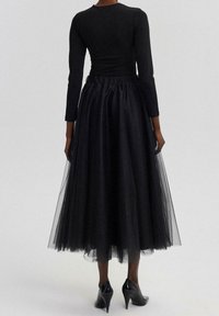 Zwarte jurk met een getailleerde lange mouwtop en een volumineuze tule rok. Voorzien van een geraffineerde tailleband en hoge hakken.