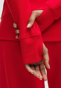 Červený top s dlouhým rukávem a žebrovanými manžetami s otvory pro palce, v kombinaci s odpovídajícím spodním dílem. Hladká textilie s přiléhavým střihem.