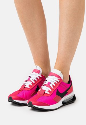 Zapatillas deportivas rosas con cordones blancos, detalles en negro y un cuello acolchado. Presentan una parte superior de malla lisa, texturas contrastantes y una suela acolchada.