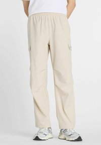 Pantalones cargo beige claro con una cintura elástica, dos bolsillos laterales y pierna ajustada, hechos de una tela suave y ligera.