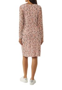 Langärmliges Kleid aus durchsichtigem pinken Stoff mit floralem Muster, knielang. Kombiniert mit weißen Sneakers, die einen lässigen Fit zeigen.