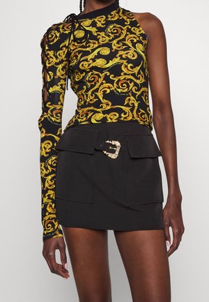 Haut noir sans manches avec motif baroque jaune et une seule manche longue à lacets, associé à une mini-jupe noire avec boucle de ceinture décorative.
