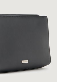 Čierna kožená kabelka s hladkou textúrou, obdĺžnikovým tvarom a striebornou logom doskou Calvin Klein na prednej strane.
