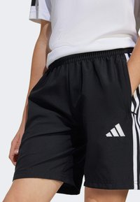 Black athletic shorts with an elastic waistband, featuring a white Adidas logo and side stripes. Smooth fabric texture, standard fit.