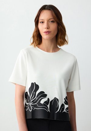 Witte korte mouwen top met een contrasterend zwart bloemenontwerp langs de zoom. Zachte textuur met een ronde halslijn.