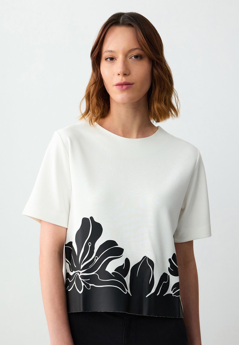 Witte korte mouwen top met een contrasterend zwart bloemenontwerp langs de zoom. Zachte textuur met een ronde halslijn.