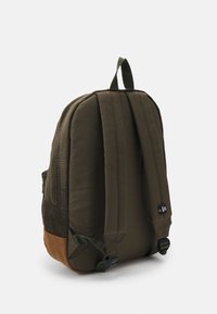 Sac à dos en tissu vert avec une finition texturée, des bretelles rembourrées, un fond marron et une poignée supérieure. Présente un petit logo noir sur le côté.