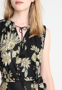 Musta mekko, jossa on keltainen ja valkoinen kukkakuosi. Varustettu nauhakiinnityksellä, jossa on musta tupsu, ja se on vartalonmyötäinen vyötärö. Sileä kankaan rakenne.