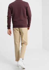 Felpa bordeaux con colletto a girocollo e polsini a coste, abbinata a pantaloni tapered beige chiaro e sneakers bianche. Design semplice e moderno.