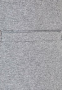 Tissu gris clair avec une texture lisse et une petite poche cousue sur le côté arrière droit.