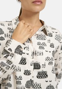 Button-up shirt made of light fabric with a cream background, featuring a black print of cosmetic items and handbags in various styles.