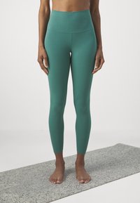 Výrazne vysoké teal legíny vyrobené z hladkej, elastickej látky. Disponujú priliehavým strihom, ktorý siaha až po členky. Žiadne viditeľné logo ani vzory.