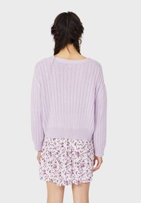 Pull côtelé lavande avec encolure large et manches longues, porté sur une jupe blanche à motifs floraux avec des accents violets. Tissu texturé visible.
