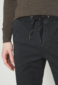 Sorte, letvægtsbukser med elastisk linning og snøre i en kontrastfarve. Har en glat tekstur og enkelt design.