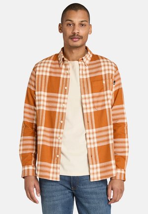 Camisa a cuadros naranja con líneas blancas y beiges, diseño de botones, bolsillo en el pecho, mangas largas, combinada con una camiseta beige clara debajo.