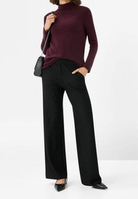 Pull à col roulé bordeaux associé à un pantalon large noir. Tissu texturé, coupe décontractée, et chaussures noires élégantes à bout pointu.