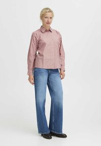Camicia a righe rosse e bianche con bottoni abbinata a jeans svasati blu chiaro e scarpe con plateau nere, indossata da un modello su uno sfondo semplice.