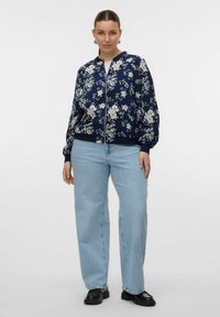 Floral bomber jacket in navy with white flowers, zip closure, ribbed cuffs, and hem. Worn with light blue wide-leg jeans and black shoes.