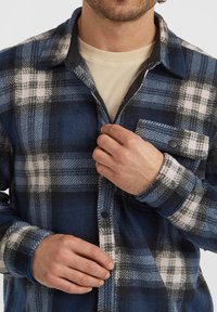 Fleece button-up shirt in marineblauw ruitpatroon met witte en zwarte accenten. Heeft een klassieke kraag, knoopsluiting en een borstzakje. Zachte textuur.