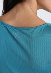 Maglietta sportiva turchese con tessuto testurizzato, scollo a giro e tre strisce riflettenti sulla parte superiore della schiena.