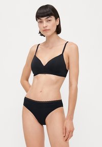 Zwarte bralette en bijpassende slipset van zacht materiaal. De bralette heeft een V-halslijn, verstelbare banden en kantafwerking; de slips hebben een vergelijkbare kantaccent.
