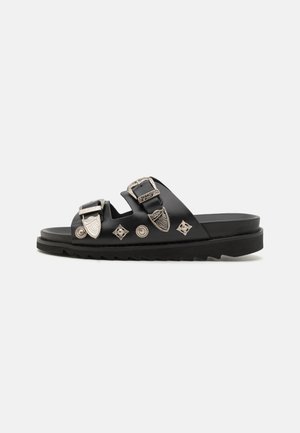 Black leather sandals with two adjustable straps, silver hardware, and decorative metallic accents. Thick black outsole with ridges.