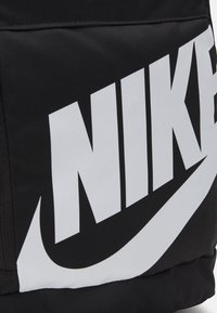 Zaino nero con un prominente logo bianco della Nike. Realizzato in tessuto resistente con una superficie liscia e dettagli di cucitura visibili.