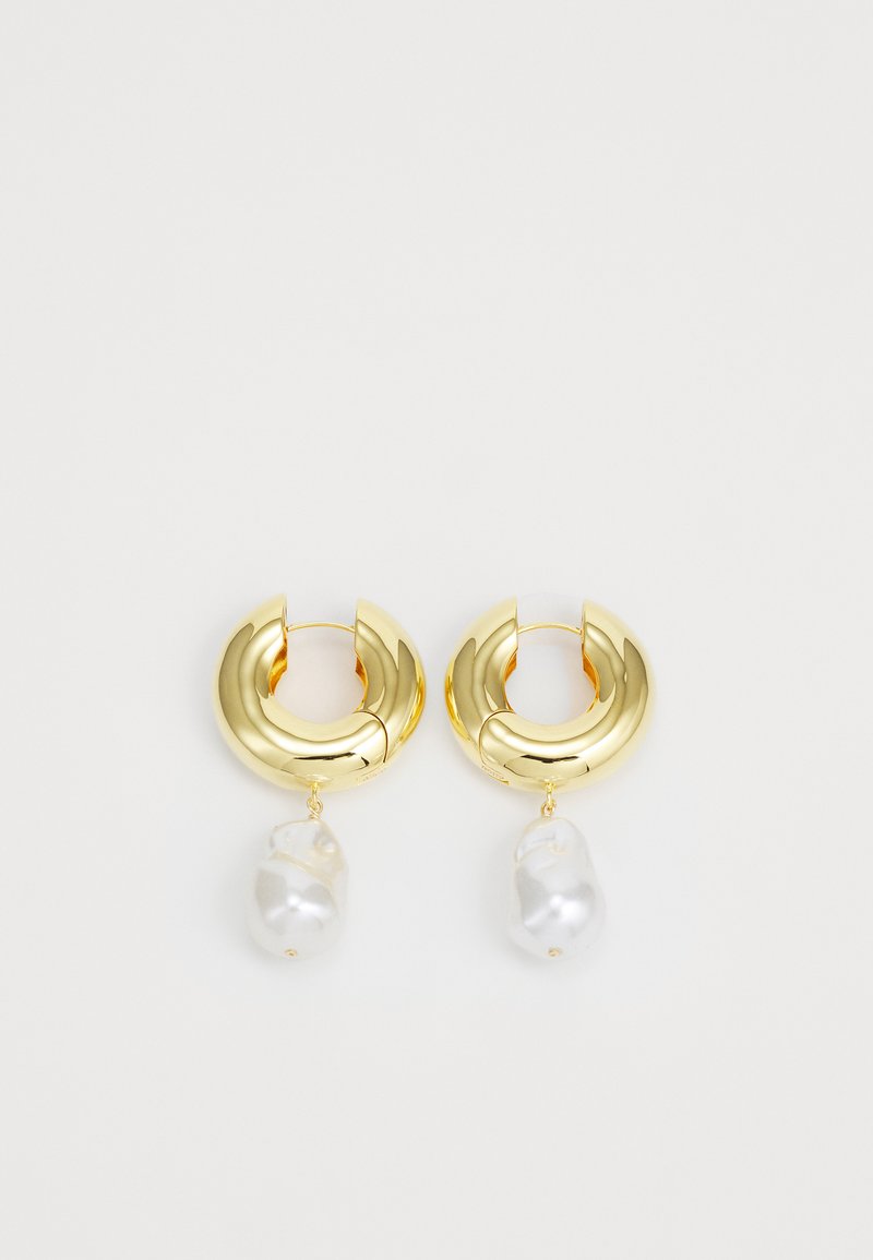 Brincos de argola em tom dourado com acabamento polido, apresentando um accent de pérola branca de forma irregular pendente. Design circular, textura suave.