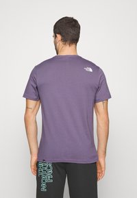 Fialové tričko s krátkým rukávem a kulatým výstřihem, na horní části zad je malé bílé logo. Materiál vypadá měkce a má normální střih.