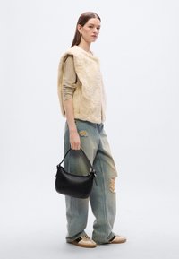 Μπεζ γιλέκο από ψεύτικη γούνα πάνω από μπλούζα με μακριά μανίκια, συνδυασμένο με ανοιχτόχρωμο τζιν με φθορές και μαύρη δερμάτινη τσάντα. Ταμπά αθλητικά παπούτσια με μαύρες λεπτομέρειες.