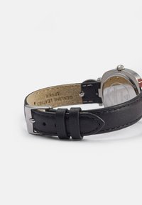 Zwart leren horlogeband met een zilveren metalen gesp, met een gestructureerd bovenoppervlak en beige voering met bedrukte details.