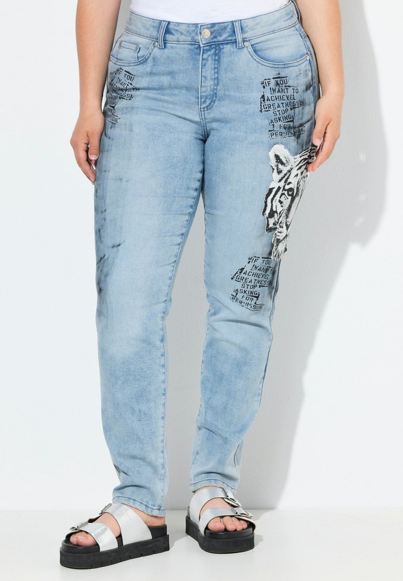 Los jeans de mezclilla azul claro cuentan con un gráfico de tigre y texto negro en la parte delantera, con un diseño ajustado y estilo de cinco bolsillos.