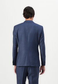 Chaqueta de traje a cuadros en azul marino con un corte ajustado, con solapas muestradas y puños abotonados, acompañada de pantalones a juego.