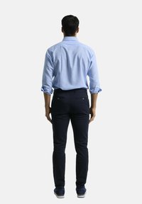 Camisa de botones azul claro, con las mangas remangadas; combinada con pantalones ajustados azul marino. Zapatos casuales con detalles texturizados. Se muestra la vista posterior.