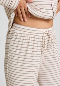 Loungebroek in roomkleur met dunne bordeauxrode strepen, elastische tailleband en trekkoorddetail. Zachte textuur, getailleerde pasvorm en casual ontwerp.